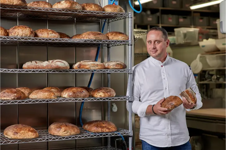 Baker from Eska Bakery holding freshly baked artisanal bread inside the bakery.